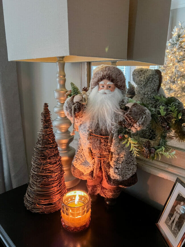 Santa with brown coat, twig tree, lamp and candle on bedside table