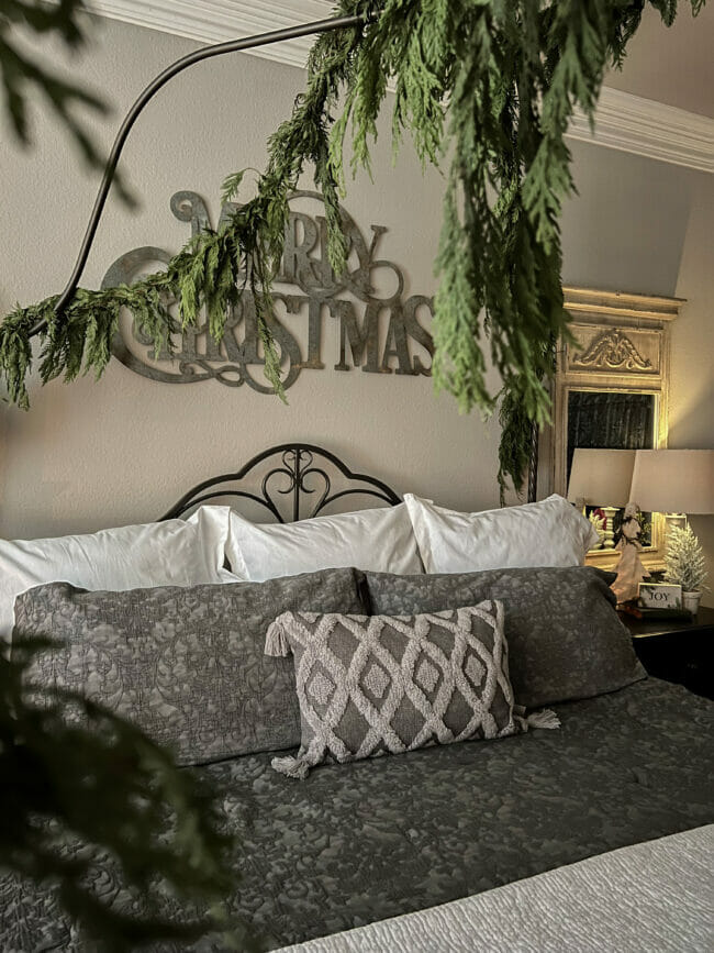 gray bedding with merry Christmas sign and greenery hanging over bed