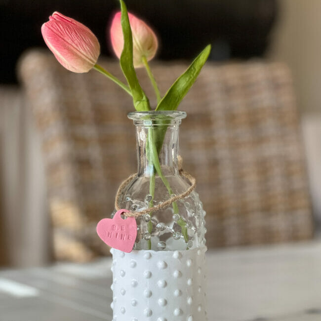 close up of glass knobby vase with pink tulip and heart
