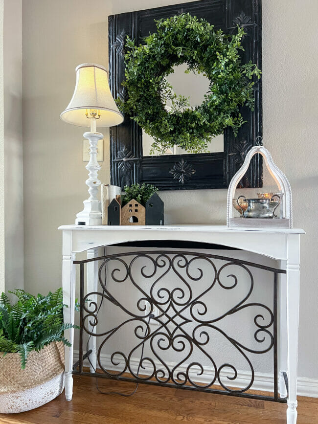 white and scrolled metal table with winter decor such as a black mirror, lamp and candles