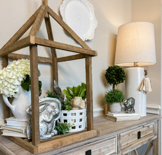 sofa table with lamp and lantern filled with silver bunnies and greenery