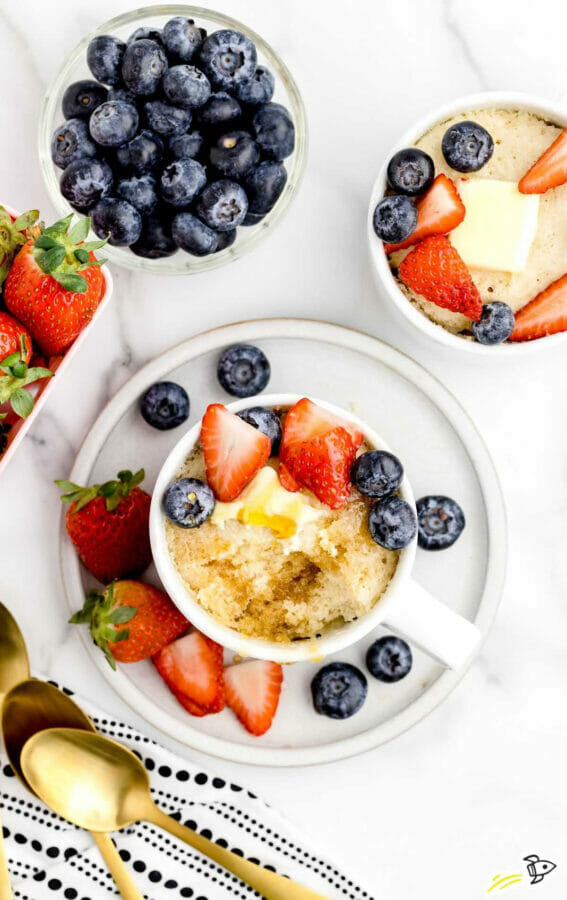 white dishes with blueberries and strawberries with a pancake in a mug