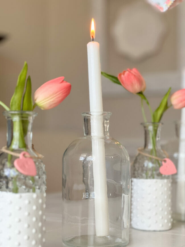 white tapered candle in jar with pink tulips in knobby vases