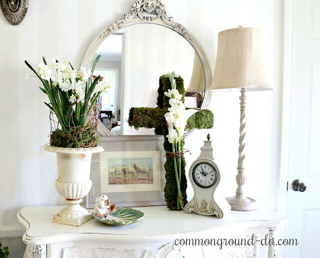 white table with green cross, lamp, urn with flowers and mirror and clock