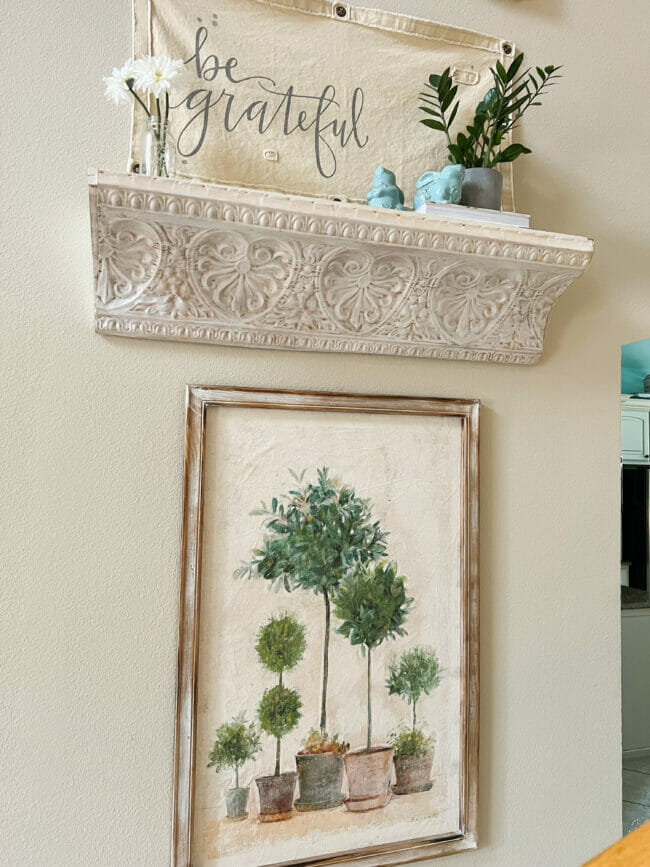 white shelf with plant and blue bunnies and topiary print hanging underneath