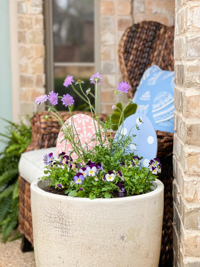 white planter with purple flower and large wooden easter eggs