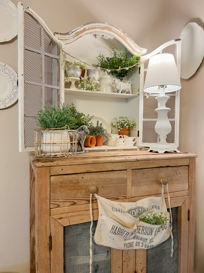 white cubby shelf with plants sitting on vintage hutch with hardware apron