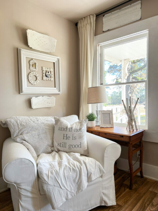 white chair in front of window with white quilt, pillow and wall decor