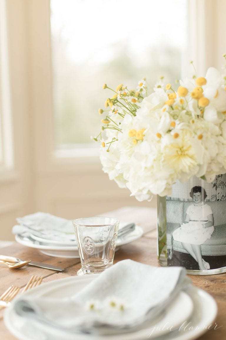 yellow and white flowers in a vase with a black and white photo at the place setting