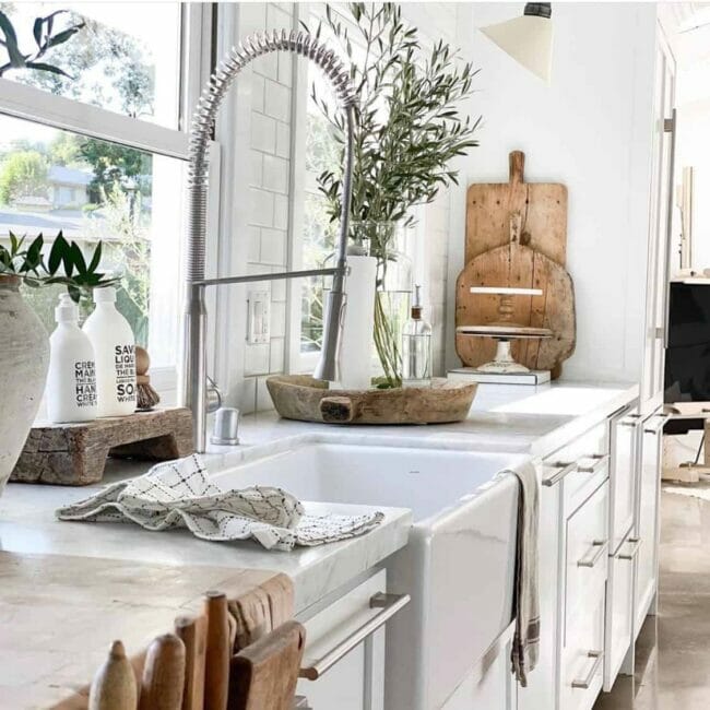 white kitchen with plants and wooden cutting boards stacked in corner