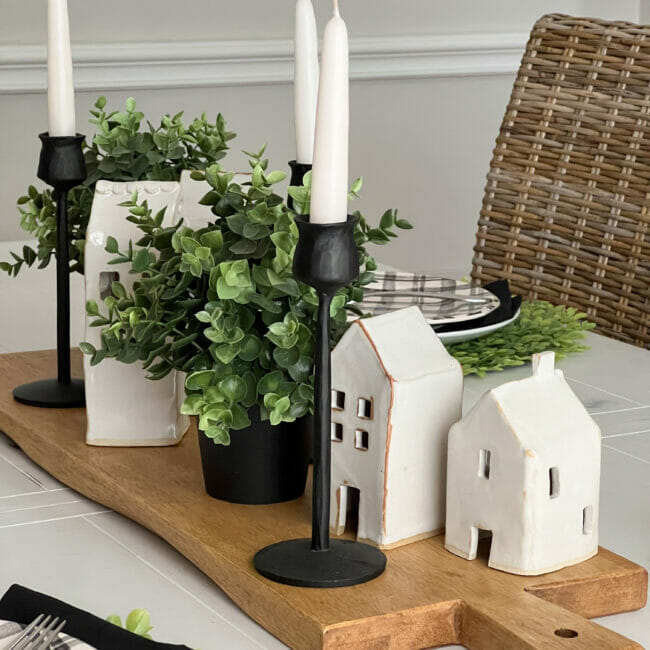 wood board with white houses, black candlesticks and boxwood