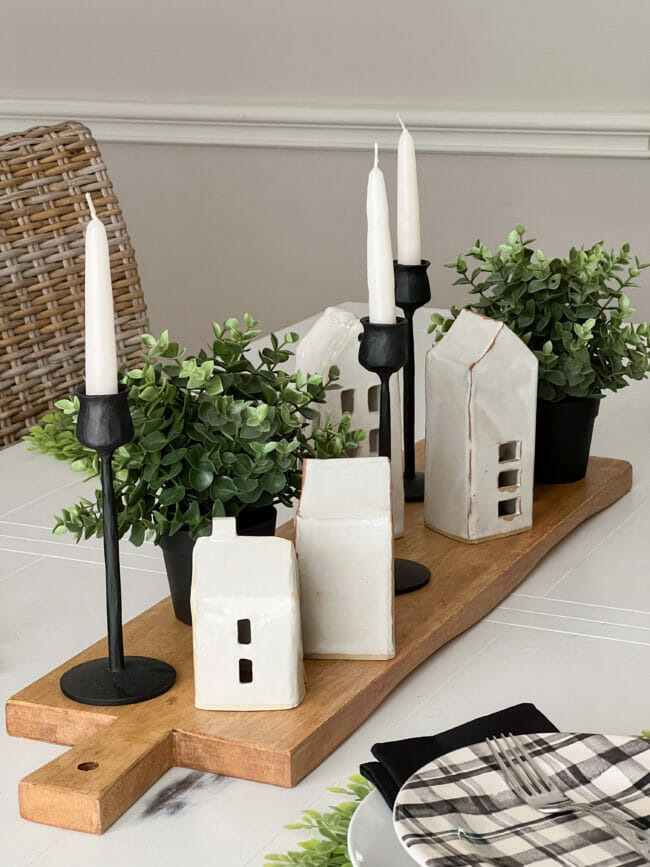 white handmade houses with boxwood and candles on top of a breadboard as a centerpiece