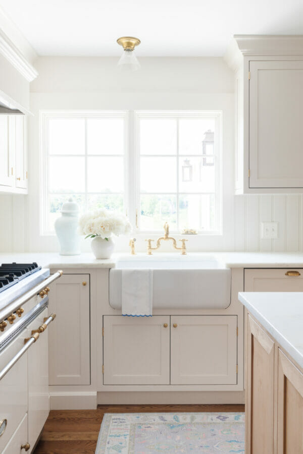white kitchen with white sink, flowers and one canister in front of window