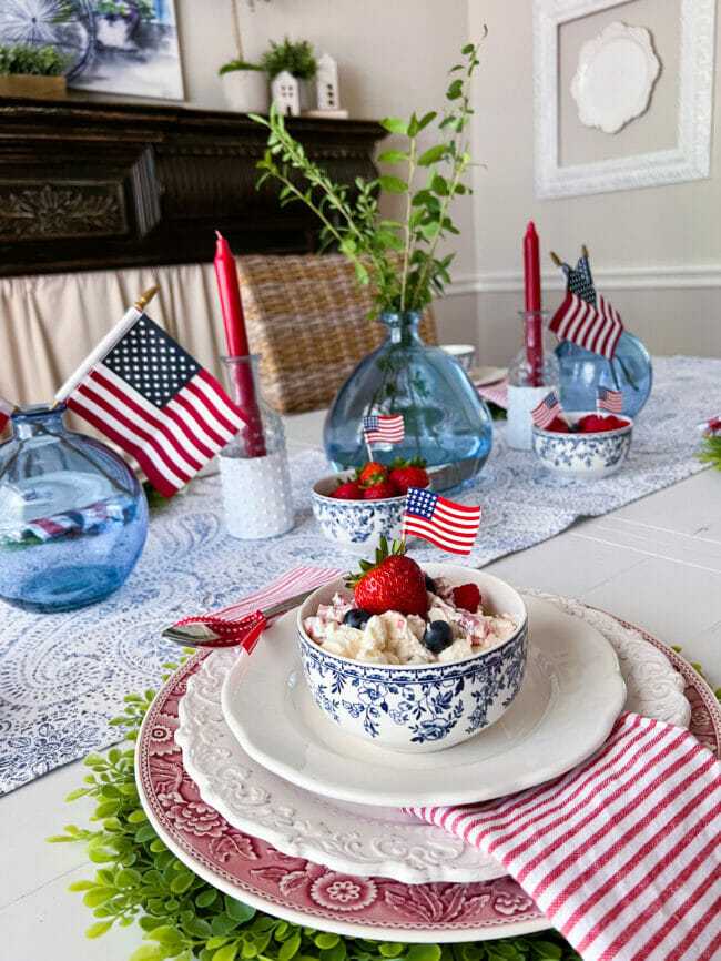 tablescape with blue jars with flags, dishes with fruit salad and red candles
