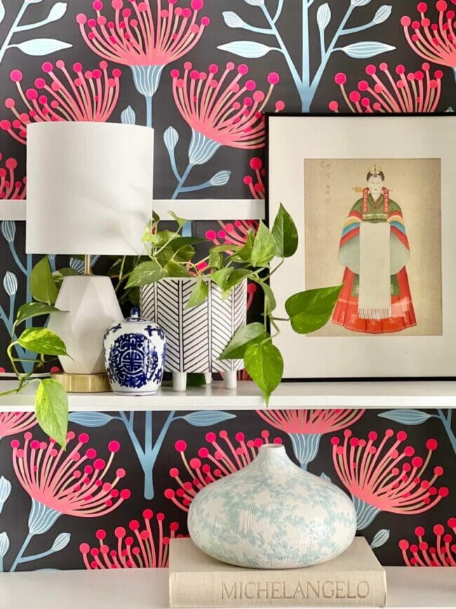 Styled book shelf with pink and blue wallpaper in background