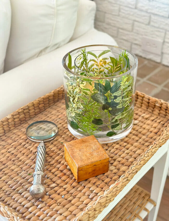 rattan tray table with green candle with greenery stems and magnifying glass