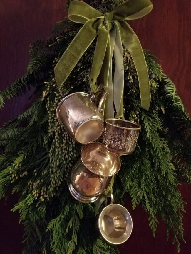 silver tray wreath hanging on door with greenery, ribbon and silver cups