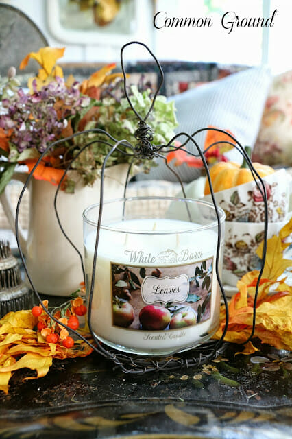 white candle and fall leaves inside a wire pumpkin