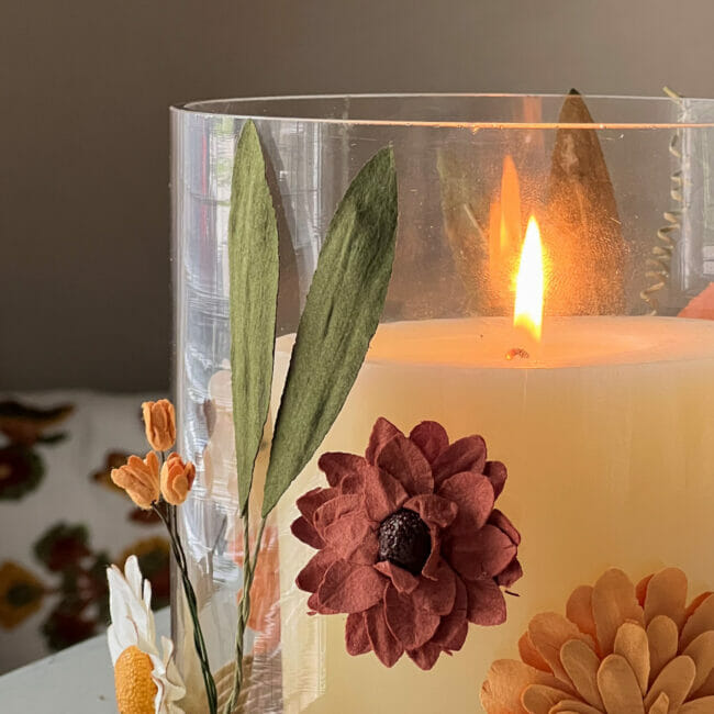close up of vase with lit candle and paper flowers in fall colors