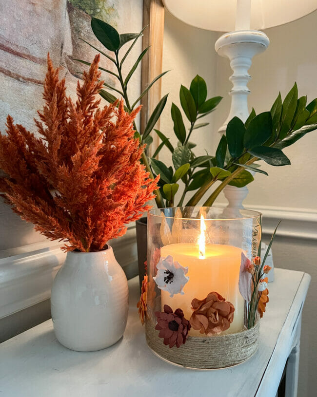 vignette with white vase with fuzzy stems, lit candle and plant
