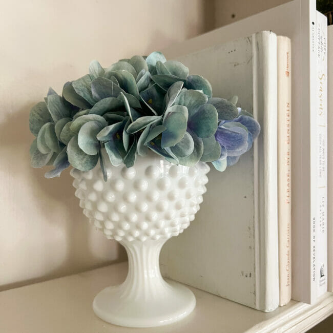 milk glass candy dish with blue hydrangea as a book end