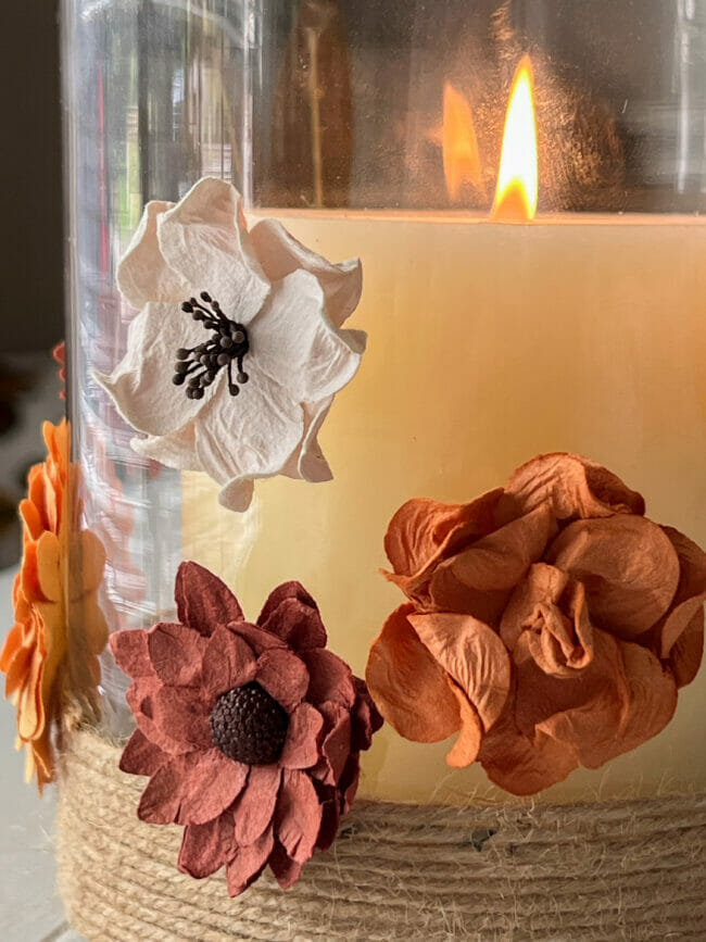 close up of paper flowers on vase with lit candle