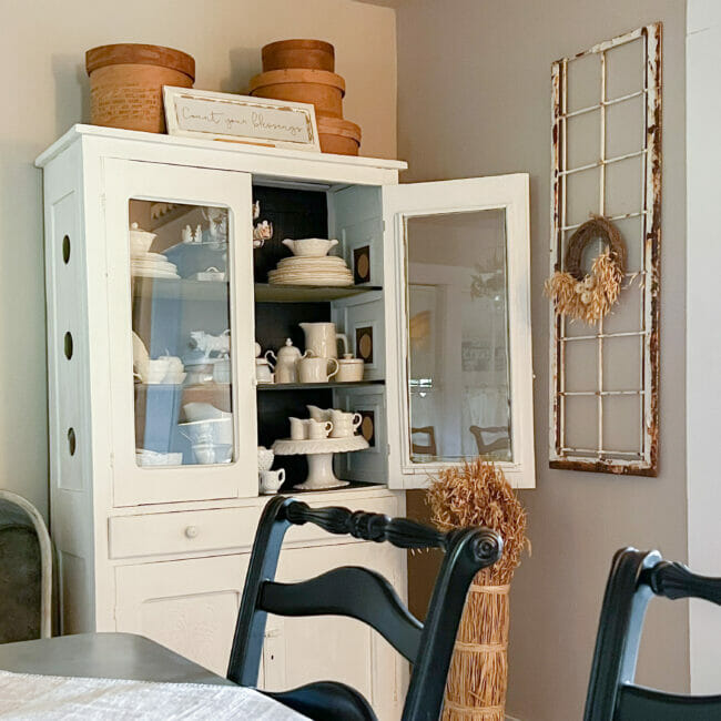 white dining hutch with white dishes and wheat bundle on floor