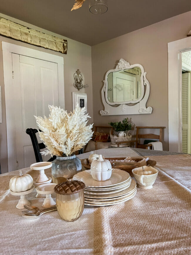 table centerpiece of white dishes, acorn candle and wall mirror in background