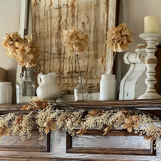 wood mantel with white and tan garland, paper flowers and white vases