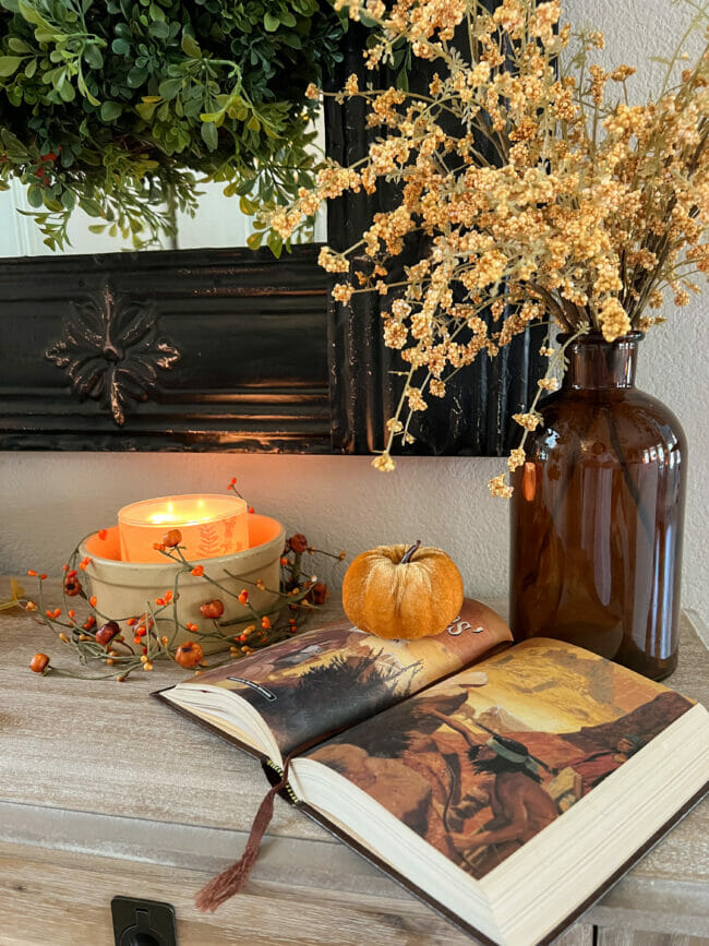 gold bowl with candle, open book, pumpkin and brown jar of stems