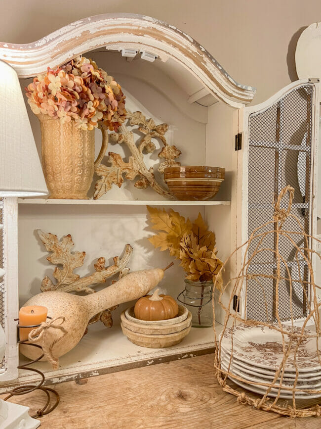 Small white decorative cabinet with fall pumpkins, leaves, gourd and pitcher with flowers