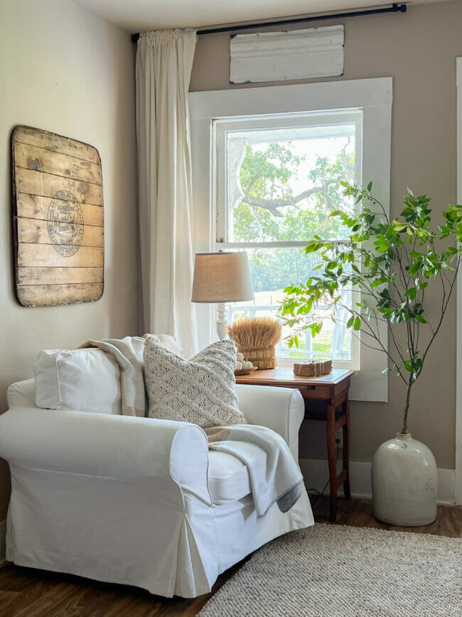 white chair, table in front of window with tall green branch in crock