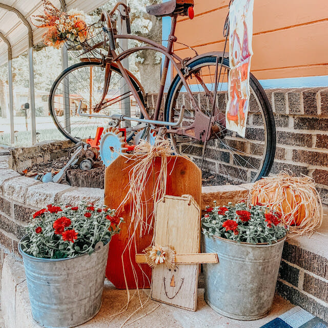 bike, fall flowers in buckets and scarecrow face made of wood