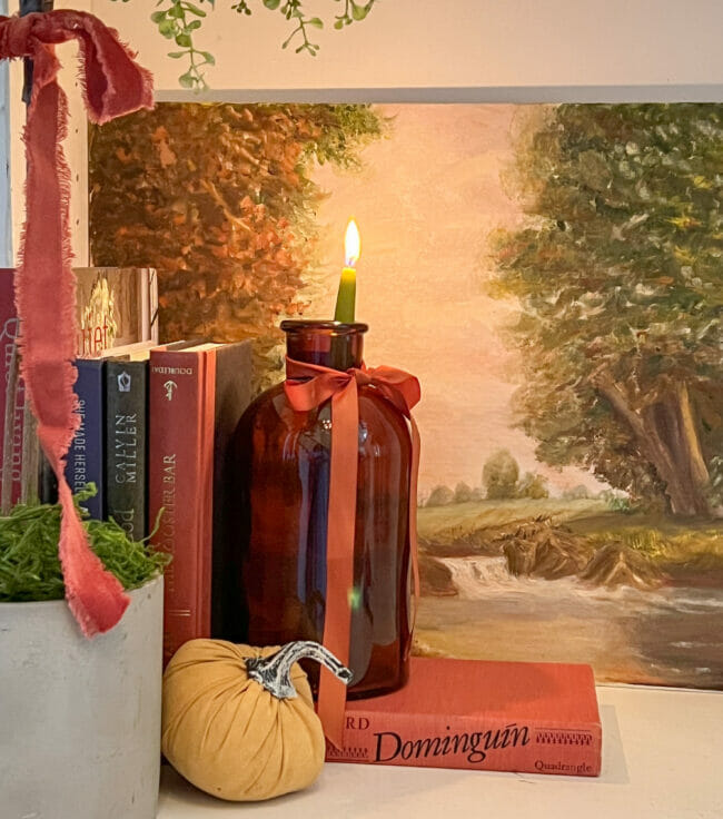 amber bottle with green candle as a bookend standing in front of a landscape print