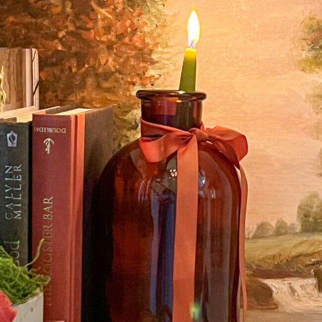 amber bottle with rust colored ribbon and a green candle with books