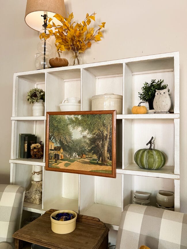 white cubby shelf with pumpkins, books, pottery and an old painting 