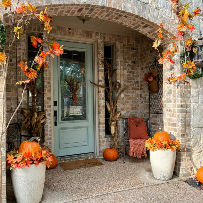 front door with pumpkins in pots, stems and cornstalks
