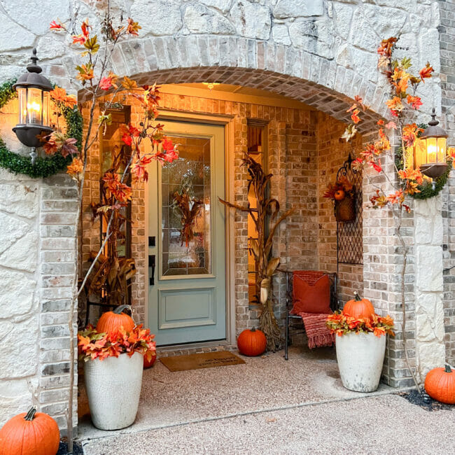 full porch with pumpkins, cornstalks and lights on