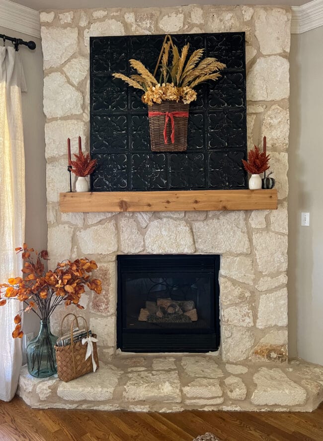 stone fireplace with black metal square piece, candles and fall stems