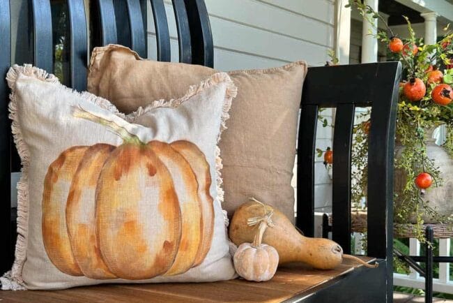 handpainted pumpkin pillow sitting with gourds on a black bench