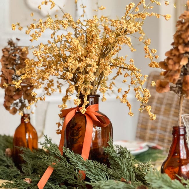 close up of brown bottles with fold stems, orange ribbon and green garland