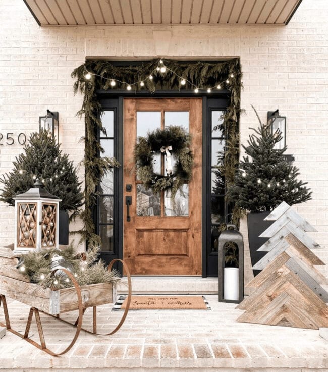 stained front door with Christmas wreath, wooden sleigh and tree on porch