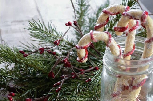 handmade candy canes in a mason jar with greenery and red berries