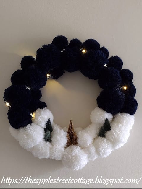 navy and white pom pom wreath with small bottle brush trees and lights