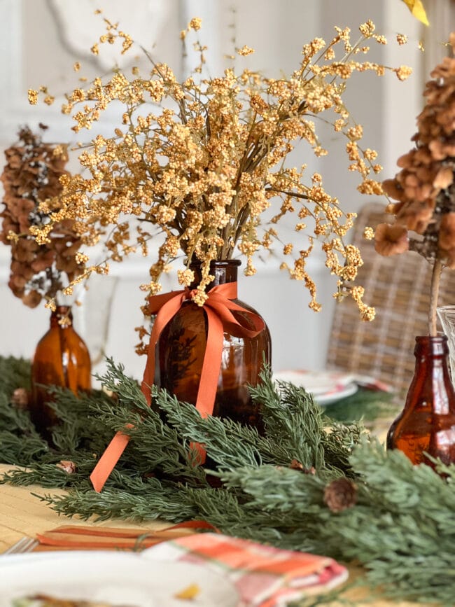 brown glass bottles with gold stems and cedar garland as a table centerpiece