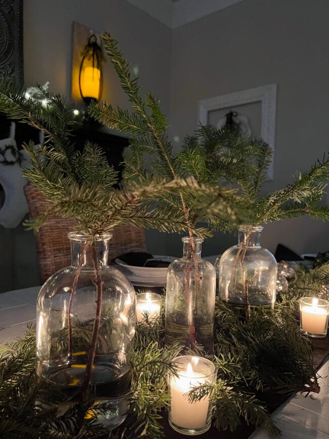 Close up of 3 clear bottles with fresh Fir stems and candles