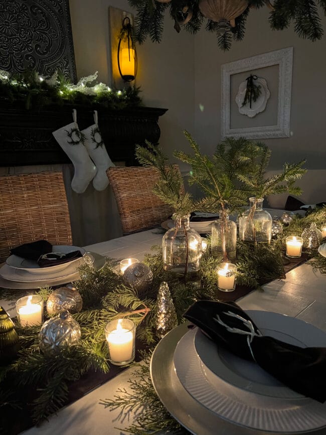 length of centerpiece with candles, fresh greenery and mantel with stockings in background