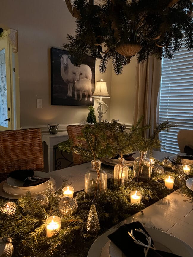 dining room table with candles, greenery hanging on chandelier and lamp and lamb print in background