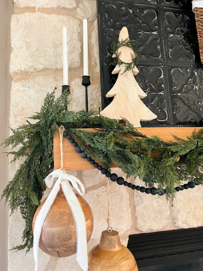 mantel with green garland, black beads, wood bells and candles
