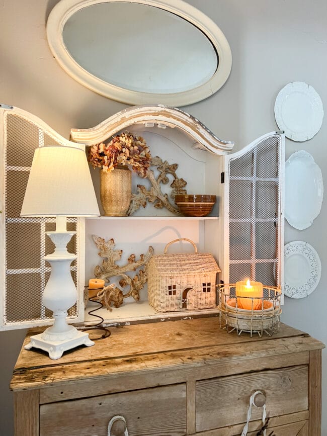 small hutch cabinet with white lamp, wicker house basket , candles and iron pieces